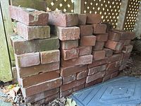 Side view of stacked red bricks showing varying conditions and sizes under an outdoor platform.