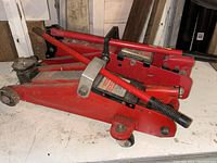 Two red hydraulic trolley jacks stacked on top of each other, showing general condition and design.