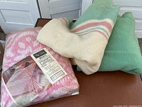 Two Kenwood wool blankets folded, and one unopened vintage Sears bedspread in plastic packaging showing label and pattern.