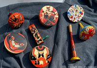 Top view of eight vintage metal noisemakers including five Halloween themed with classic 1950s graphics placed on dark background cloth.