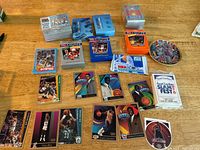Basketball card sets and mini Larry Bird plate laid out on a wooden surface showing unopened and opened packs, cards featuring players, and collectors cards.