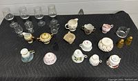 Overview of all items laid out on black padded surface showing china sets, glassware, and salt shakers