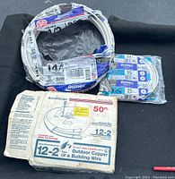 Photo showing the 50-foot box labeled American 12-2 UF-B outdoor copper building wire, a partially used spool of white 14/2 wire with Romex branding, and two smaller unopened packages of 14/3 Romex wire.
