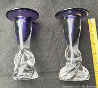 Pair of glass candlesticks showing clear body with twisted swirl at base and amethyst purple rim, placed on a dark fabric background, measuring tape nearby showing approx 6.5 inches height.