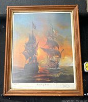 Framed print showing two historical sailing ships at sea under a colorful sky at sunset. The print is titled and signed by John Pitre.