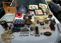 Wide photo of entire lot laid out, showing multiple items including wooden toolbox, trays, paintings, hats, model cars, and other collectibles.