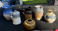 All six pottery pieces arranged on a black surface, showing variety in size, color, and shape.