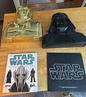 Photo showing black Darth Vader and gold C-3PO shaped toy holders with Star Wars books and music album