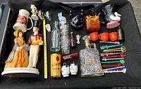 Photo showing full lot including Gibney vodka ceramic pitcher, decorative glass decanter, various vintage glass bottles, Milwaukee stein, salt and pepper shakers, miniature figurines, bowling pin bank, and many swizzle sticks.