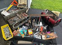 Wide view of vintage metal Craftsman mechanics toolbox open with tools inside, yellow bin of nuts and bolts, red and black Husky tool bag, and assorted hand tools on table.