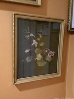 Framed textile embroidery artwork with light pink and white flowers on dark background