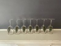 Front view of seven Spode Christmas Tree motif wine glasses with gold rim, standing upside down in a row.