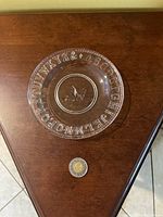 Clear shot of the antique pressed glass plate showing the alphabet embossed around the rim and bird design in center with coin for size reference.