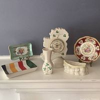Front view of the porcelain items arranged on mantle, including the clock, vases, dish, trays, and plate.