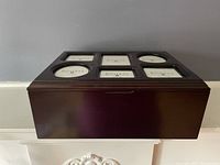 Closed view of dark wooden photo keepsake box with multiple photo frame slots on lid containing Bombay Company labels.