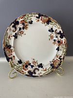 Front view of a round antique plate with floral decoration in navy, rust, green, and gold colors on white base.