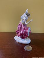 Side view of the Royal Doulton Columbine figurine with coin for size reference showing detailed paint and sculpt.