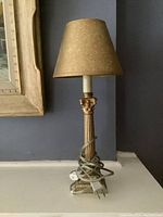 Photo of the gold boudoir lamp on a gray surface with its cord coiled around the base and a beige pleated lampshade
