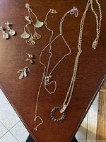 Photo showing seven pieces of jewelry on a wooden surface including multiple necklaces and earrings arranged separately.