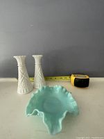 Two white hobnail and diamond hobnail pattern milk glass bud vases with ruffled tops next to a blue-green ruffled edge milk glass trinket dish