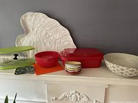 Overview of kitchen lot showing leaf tray, green fruit keeper, red bowl, red container, striped ceramic bowls, and grey basket