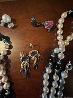 Top close-up photo showing details of Monet dangling earrings with purple beads, reversible Swarovski pearl earrings, and parts of the multi-colored pearl necklaces.