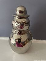 Front view of the silver metal snowman cocktail shaker showing smooth reflective surface and scarf detail at the neck.