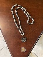 Full view of the pearl necklace with dark semi-precious beads and rectangular pendant, laid on wood surface with a coin for scale.