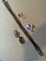 All jewellery items displayed on a flat surface: dark wrap bracelet, earrings, brooch, and shoe clips.