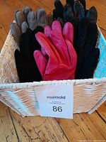 Six pairs of gloves in white wicker basket on wood floor, with MaxSold tag