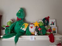 Wide view of lot displayed on a white shelf showing large Grinch plush sitting with smaller Grinch and duck animatronics, ornaments, and stocking.