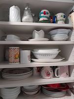 Shelf view showing Corelle Herb pattern plates, Blue Garland bowls, ceramic gravy boat, glass syrup dispenser, melamine kids mugs and other ceramic dishes.