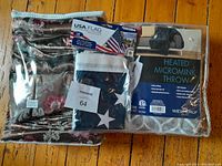 Curtain panels, American flag in original packaging, and heated micromink throw blanket sealed in package on hardwood floor