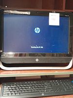 HP Pavilion 20 all-in-one desktop powered on with HP logo visible on screen, also showing HP keyboard below.