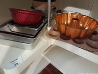 Photo showing stack of kitchen bakeware including copper bundt pan, red square pan, and rectangular metal pans