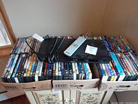 Full view of three boxes filled with DVD movie cases, with a Sony DVD player and cables placed on top.