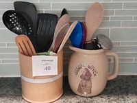 Two ceramic canisters side by side on countertop, containing assorted kitchen utensils