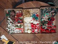 Three trays of assorted vintage Christmas decorations including beaded bells, crochet ornaments, bottle brush trees, metal candle holders, poinsettias, wreaths, and packaged charms.