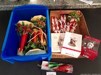 Blue container with three electric Beacon red foil candles with faux greenery, box with three boxed Nightmare Before Christmas Hallmark ornaments, other loose foil ornaments and small red umbrella foil ornament in box.