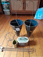 Overall lot showing pair of black metal umbrella stands, wire hat holder, wall-mounted card holder, decorative metal piece, and vintage tin on wood floor