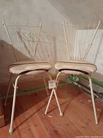 Full view of the pair of vintage iron side chairs with cushioned seats positioned on a wooden floor against a wall.