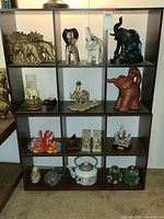 Dark wood 6-cube cubby shelf filled with elephant-themed bookends, various elephant figurines, teapots, snowglobe, and other decorative collectibles.