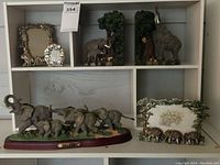 Shelf displaying the resin elephant bookends on the right, three pewter and enamel elephant picture frames on the left and center top shelf, and the Classic Wildlife Collection Elephant Herd Sculpture on the lower shelf.