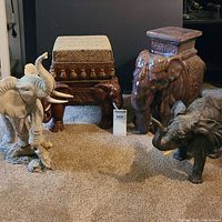 Lot showing all items together: ceramic elephant stand, wooden stool with padded cushion, and two resin elephant figurines on carpeted floor.