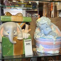 Front view of two Disney themed ceramic cookie jars, one Dumbo in a bathtub and one gift box with Disney characters.