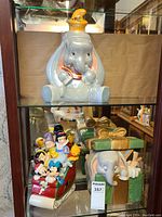 Wide view of display cabinet with three Disney cookie jars: pearlescent Dumbo, Christmas sleigh with Disney characters, and Disney character box.
