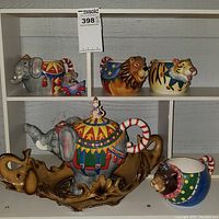 Photo showing the full circus animal ceramic tea set and wooden tray on a white shelf with lot number tag.
