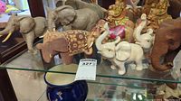 Set of nine elephant sculptures arranged on a glass shelf showing both large gray Lenox elephants and smaller elephants in various styles and colors.