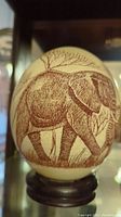 Ostrich egg etched with an elephant image in red-brown color, mounted on wooden stand.