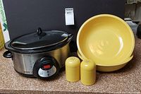 Photo of all items together: Crock-Pot slow cooker, two yellow Fiesta serving bowls, yellow salt and pepper shakers on countertop.